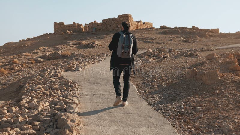 El turista europeo casual camina a las ruinas antiguas El hombre relajado en el camino del desierto del verano toma una foto del