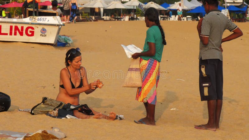 El turista europeo se sienta en la playa enfrente del vendedor local marrón