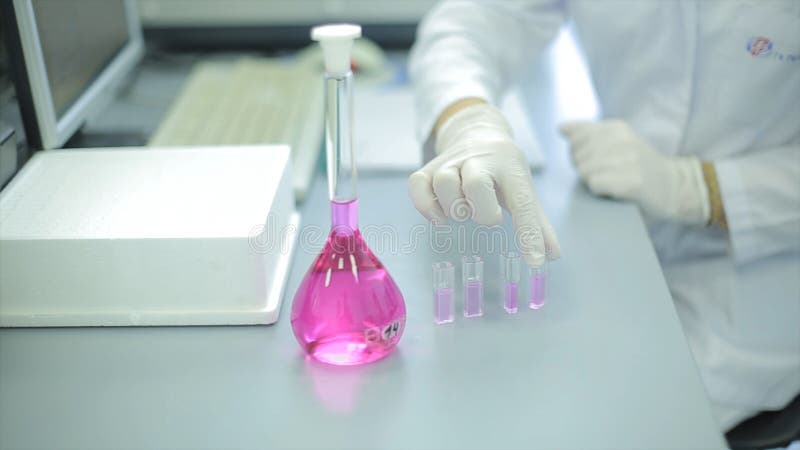 El técnico de laboratorio de sexo femenino joven que examinaba un frasco de Erlenmeyer de cristal cónico llenó de una solución lí fotos de archivo El técnico de laboratorio de sexo femenino joven que examinaba un frasco de Erlenmeyer de cristal cónico llenó de una solución lí fotos de archivo
