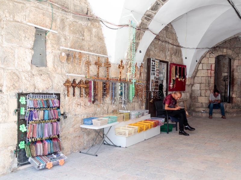 El vendedor de la tienda de los recuerdos de la iglesia se sienta y mira en su teléfono móvil en la ciudad vieja de Jerusalén, Is fotografía de archivo El vendedor de la tienda de los recuerdos de la iglesia se sienta y mira en su teléfono móvil en la ciudad vieja de Jerusalén, Is fotografía de archivo