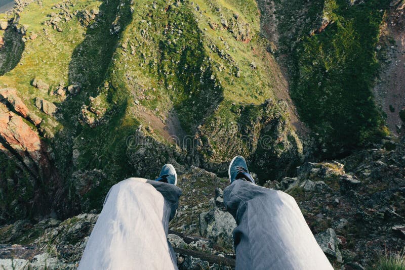 El viajero se sienta al borde de un acantilado Pies del hombre en el fondo de un paisaje de la montaña Concepto de aventura y de fotografía de archivo libre de regalías El viajero se sienta al borde de un acantilado Pies del hombre en el fondo de un paisaje de la montaña Concepto de aventura y de fotografía de archivo libre de regalías
