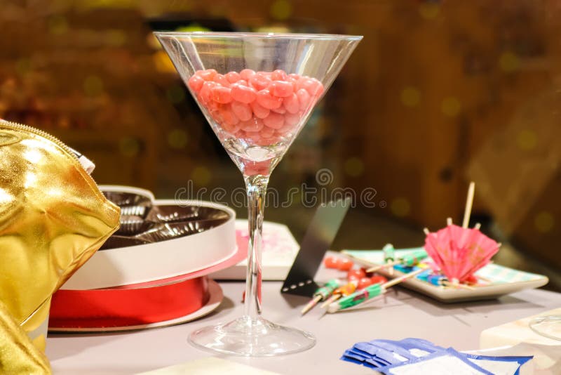 El vidrio de Martini llenó de los jellybeans rosados en la tabla con los paraguas dispersados y sobre todo la caja vacía del choc imagen de archivo El vidrio de Martini llenó de los jellybeans rosados en la tabla con los paraguas dispersados y sobre todo la caja vacía del choc imagen de archivo