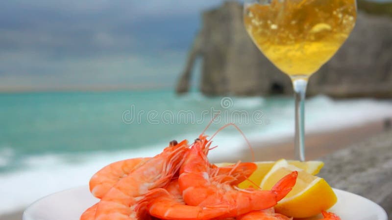 El vino blanco se vierte en un vaso con gambas y limón al fondo