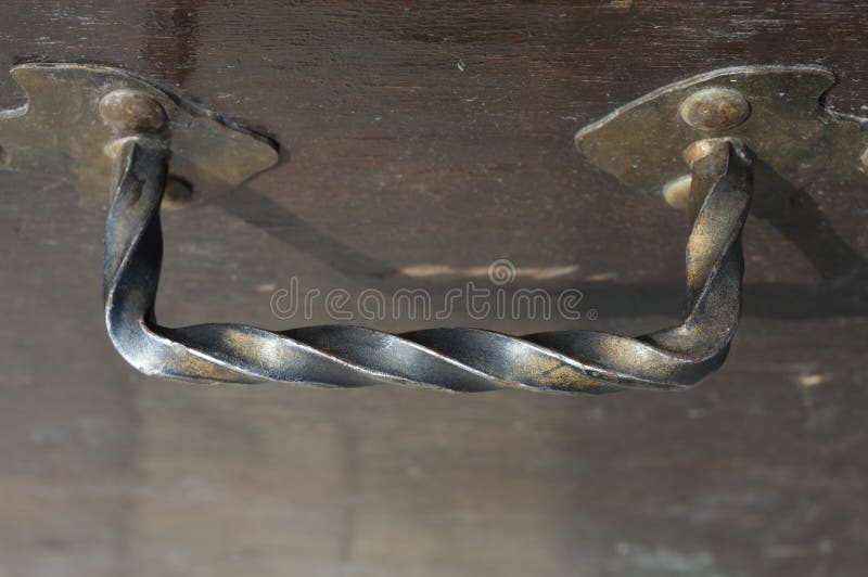 Close of weathered iron handle attached to a wooden surface. Handle is hand made, hammered and twisted. Close of weathered iron handle attached to a wooden surface. Handle is hand made, hammered and twisted.