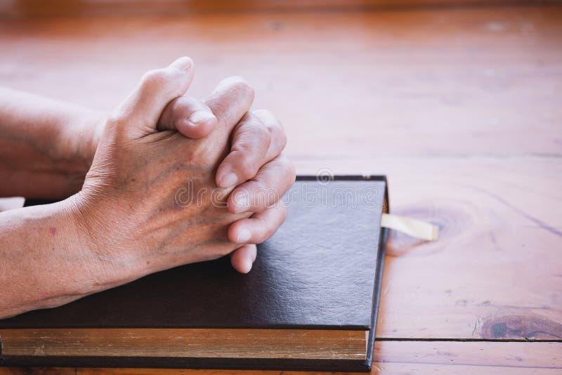 Elder woman hands folded in prayer on a Holy Bible