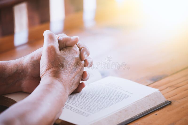 Elder woman hands folded in prayer on a Holy Bible