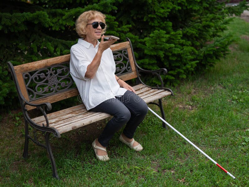 Elderly Blind Woman Talking on a Smartphone while Sitting on a Bench in