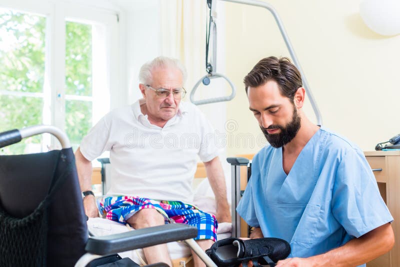 Elderly care nurse helping senior from bed to wheel chair in hospital or nursing home