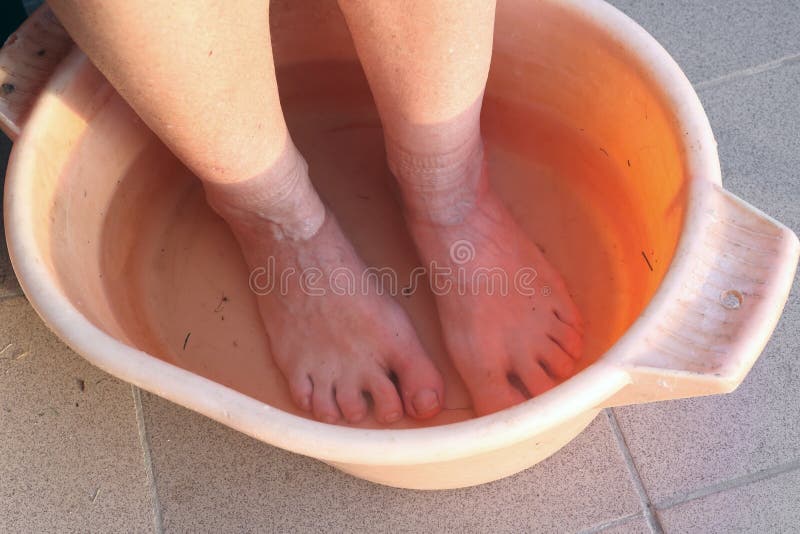 An elderly country woman washing her dirty feet in an orange plastic basin