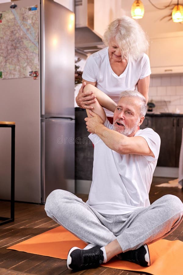 elderly couple exercising at home, woman help husband to stretch royalty free stock images