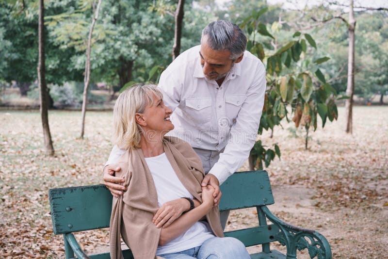 Elderly couple sitting on a bench showing love by hugging together at the public park in the morning. Happy concept of lifestyle. In the retirement stock images Elderly couple sitting on a bench showing love by hugging together at the public park in the morning. Happy concept of lifestyle. In the retirement stock images