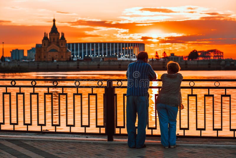 Elderly couple standing back on the river bank and watching the sunset
