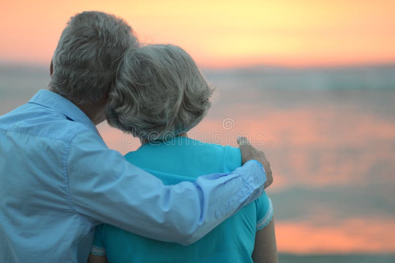 Coppia di anziani in amore al tramonto in una sera d'estate a guardare il mare.