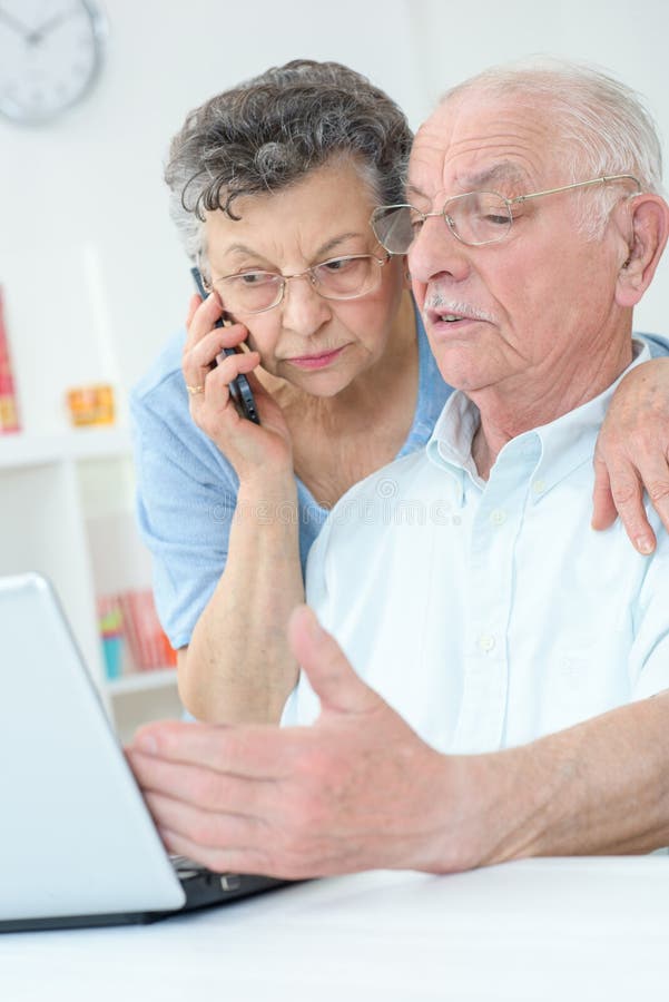 Elderly couple using laptop wife on telephone royalty free stock photo
