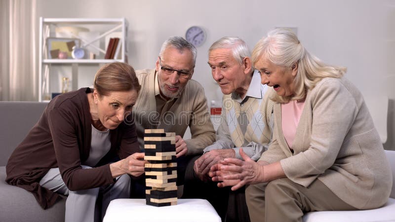 Elderly friends building tower from wooden cubes leisure time in nursing home stock photo Elderly friends building tower from wooden cubes leisure time in nursing home stock photo