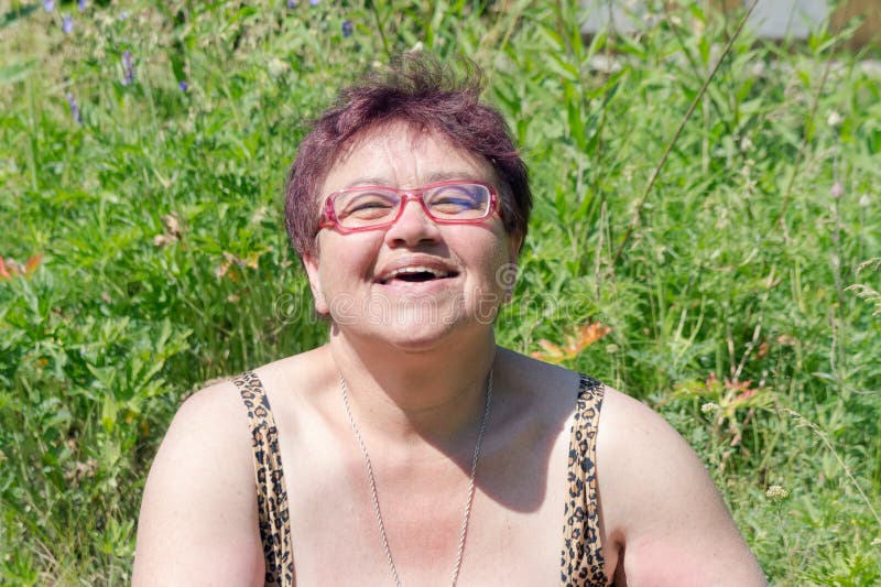 Elderly happy woman with glasses sunbathes in the grass under the bright summer sun stock photo Elderly happy woman with glasses sunbathes in the grass under the bright summer sun stock photo