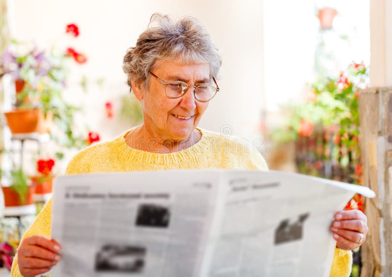 Elderly home care. Elderly woman sitting on the veranda and reading newspaper royalty free stock images