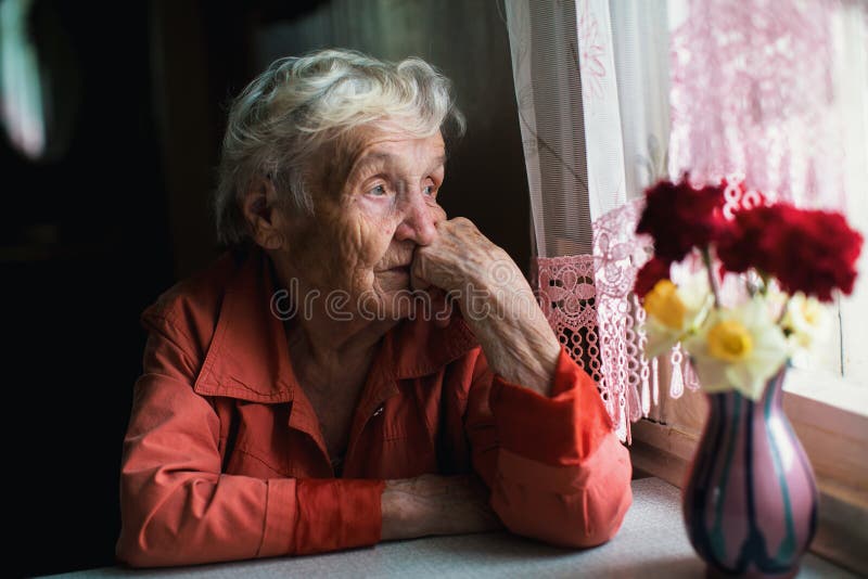 Elderly lone woman looks sadly out the window.