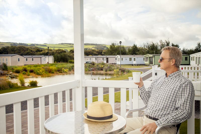 Elderly man drinking a mug of coffee sitting on the veranda of a stock image