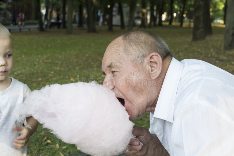 An Elderly Man With His Mouth Wide Open Greedily Bites Cotton Candy