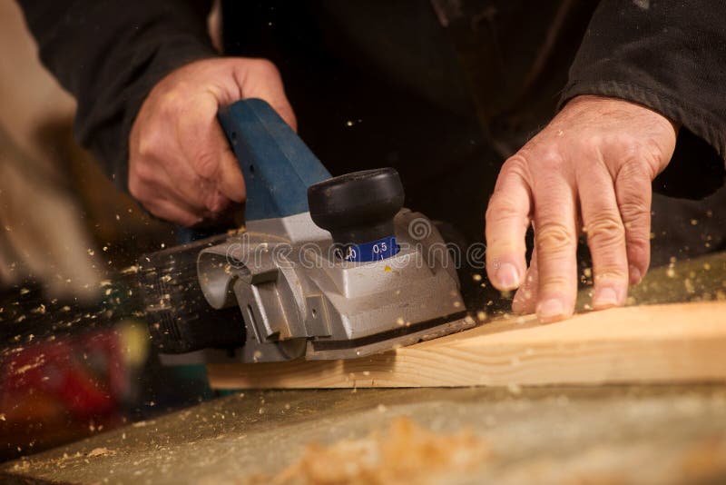 Close up of the hand of an elderly man planing a plank of wood in his carpentry workshop with a plane to smooth the surface