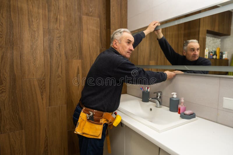 An Elderly Man Repairs a Bathroom Mirror. Stock Photo Image of home