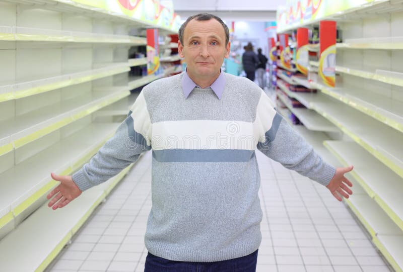 Elderly man stands between empty shelves in shop stock photo Elderly man stands between empty shelves in shop stock photo