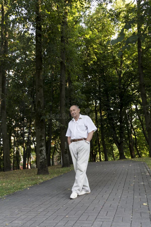 An elderly man walks alone in the park in the summer. Portrait of an old man who is alone in the park among the trees.