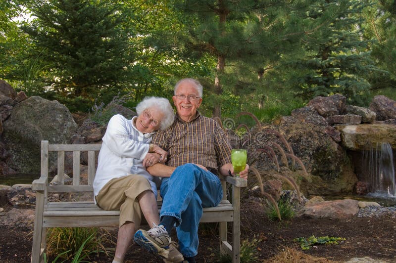 Senior man and woman sitting on a bench by a man-made pond and waterfall. Man made waterfall stock images, royalty-free photos and pictures
