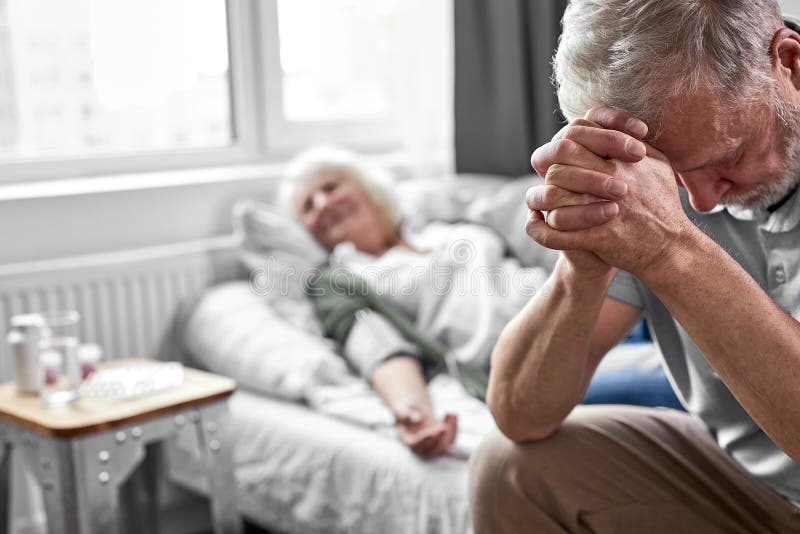 elderly man crying and mourning the loss of his wife, sitting by her side royalty free stock photos