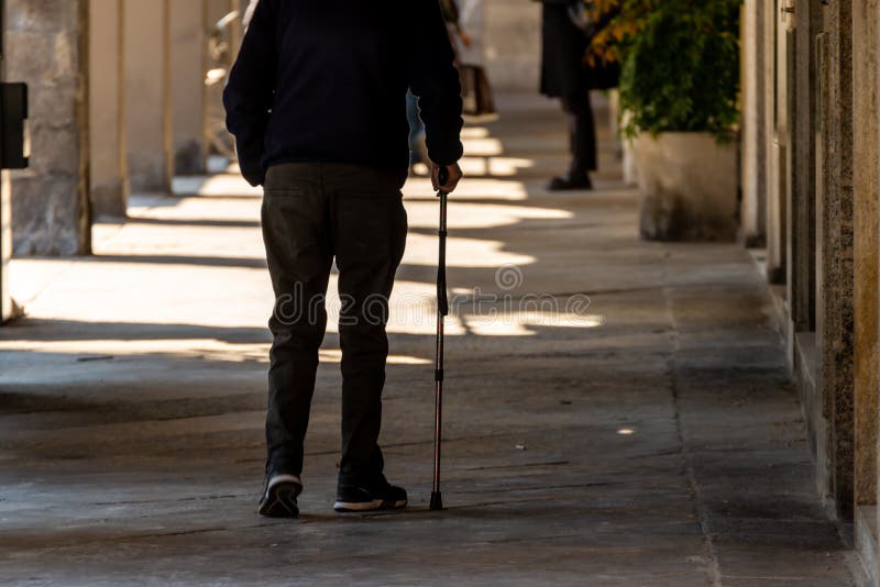 Silhouette of man walking with a cane, long shadow on pavement. Concept of  blind person, disability, old age, diseases of the spine Stock Photo