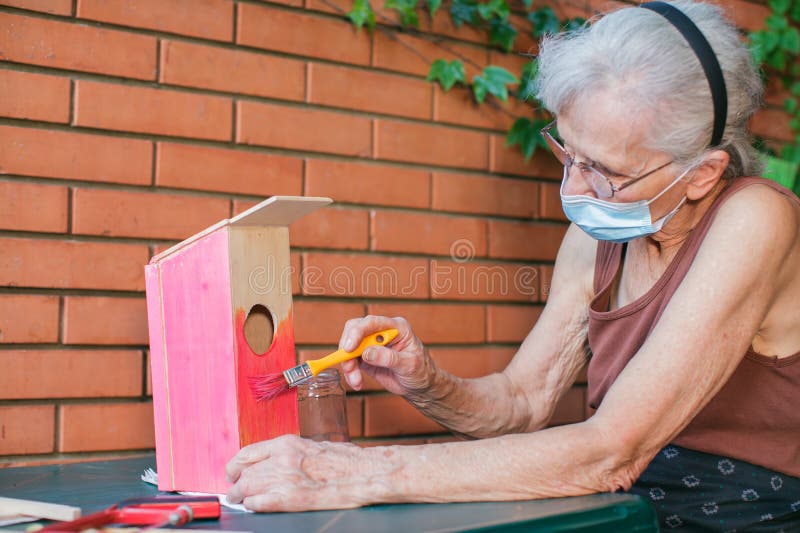 old woman with face mask painting a birdhouse