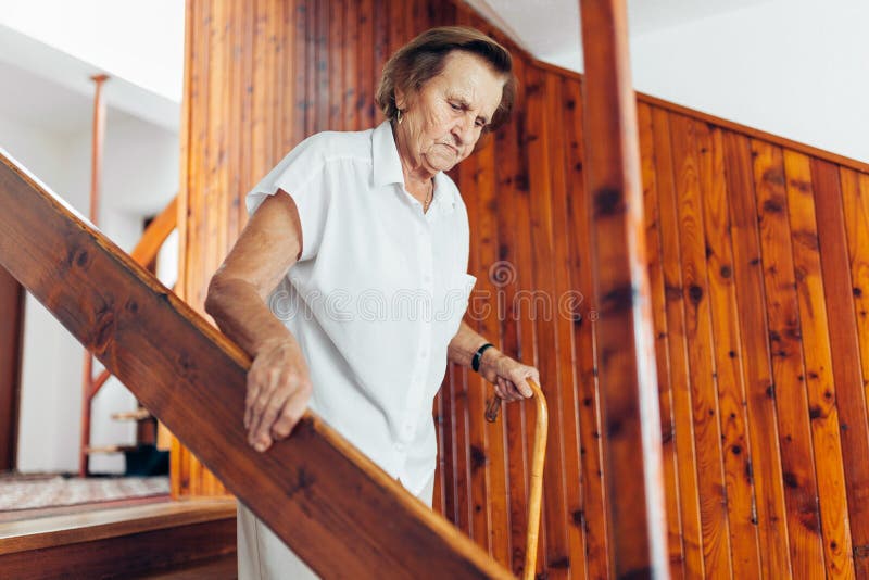 Elderly woman at home using a cane to get down the stairs