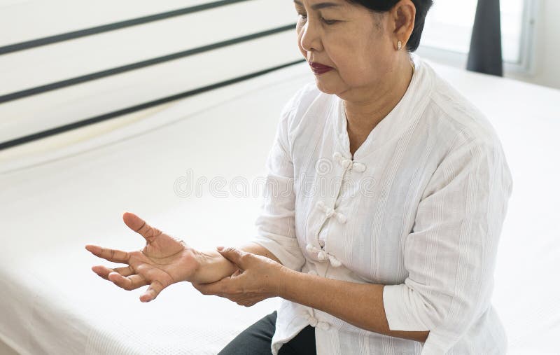 Elderly woman looking her hand and suffering with parkinson`s disease symptoms