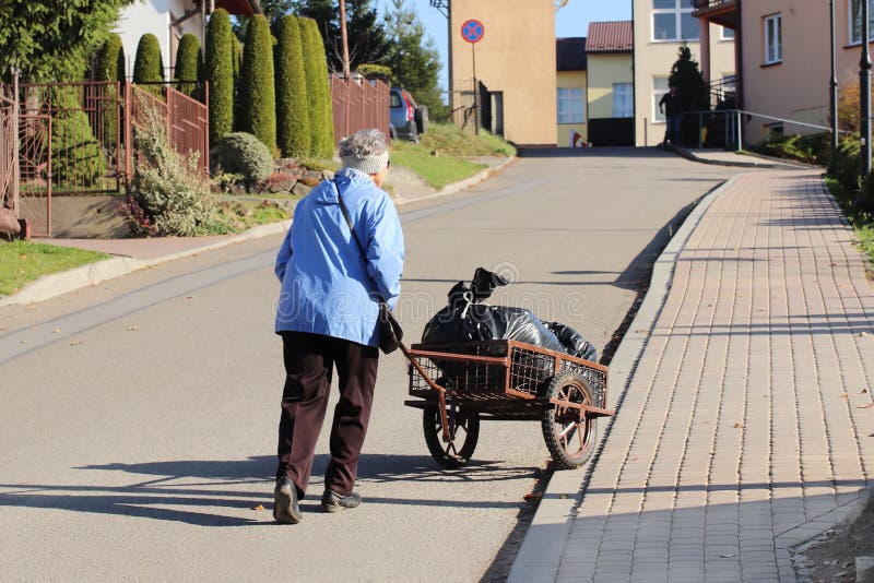 An elderly woman is pushing a wheelbarrow with a package of garbage in front of her. Removal of household waste. Ordinary life on royalty free stock photos An elderly woman is pushing a wheelbarrow with a package of garbage in front of her. Removal of household waste. Ordinary life on royalty free stock photos