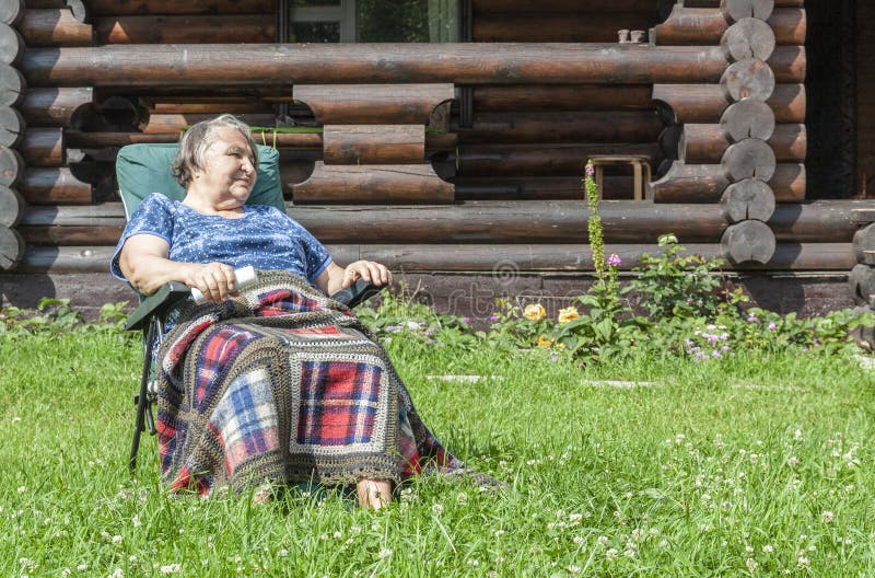 An elderly woman sitting in a chair on the lawn in front of the house. As a background royalty free stock images