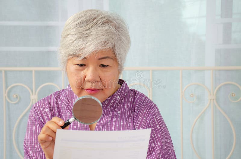 Elderly woman using a magnifying glass to reading through the lens to handheld document as her eyesight deteriorates with age