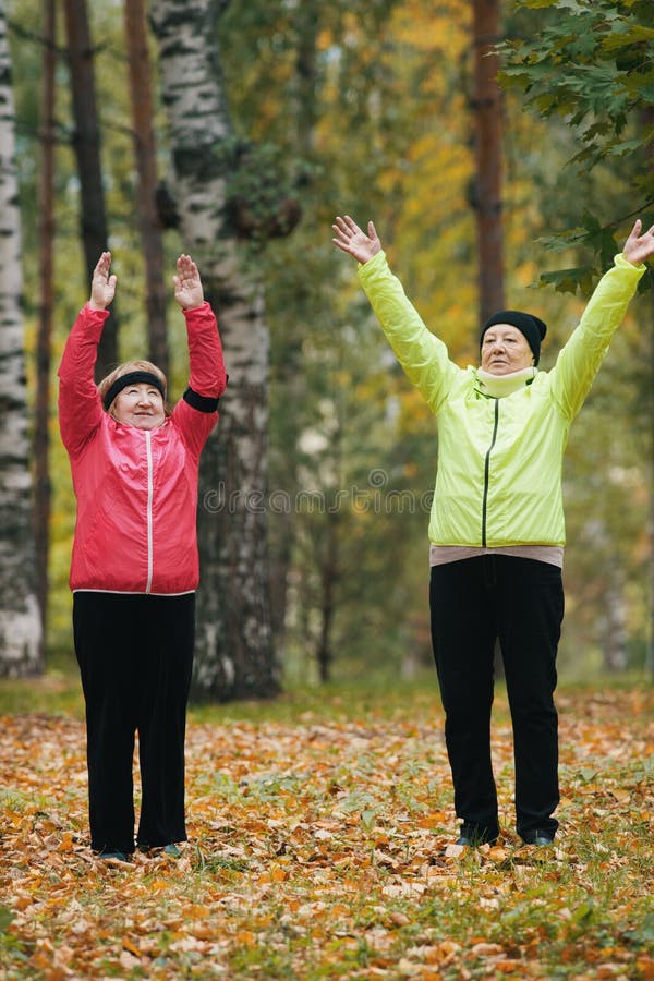 Elderly women perform a warm-up and raise their hands up in the autumn park after a scandinavian walk