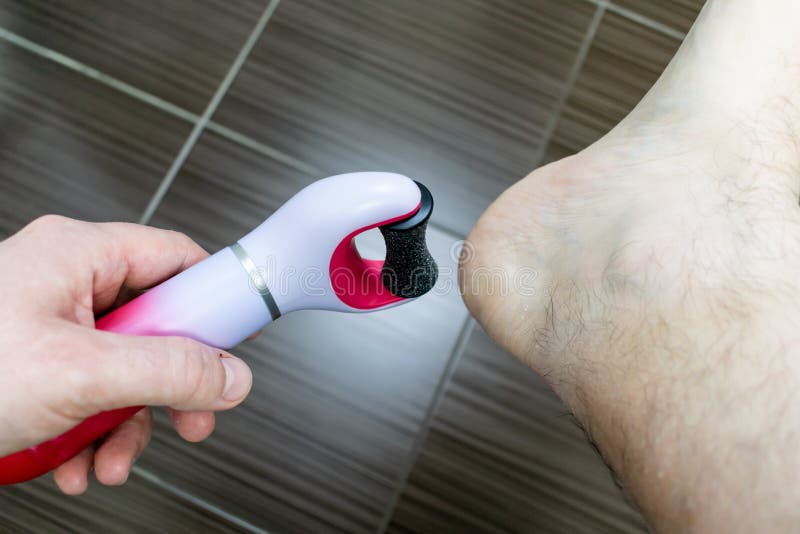 The main subject is out of focus, electric callus remover machine closeup remove old skin care treatment male hand hold bathroom