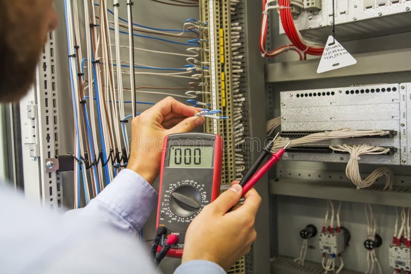 Electrician engineer with multimeter tests electrical control panel of automation equipment. Specialist in the Controller cabinet. stock photos