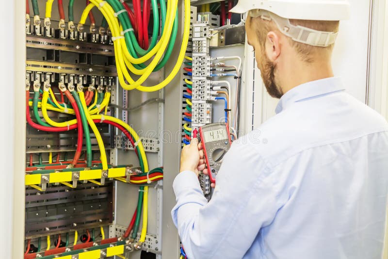 Electrician engineer in white helmet tests power voltage panel of three phase circuit. Service engineer electric with multimeter. royalty free stock photo