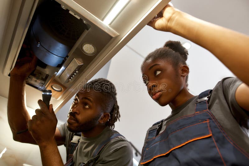 Electricista experimentado explicando a una joven aprendiz cómo arreglar los problemas de agotamiento de la cocina fotografía de archivo