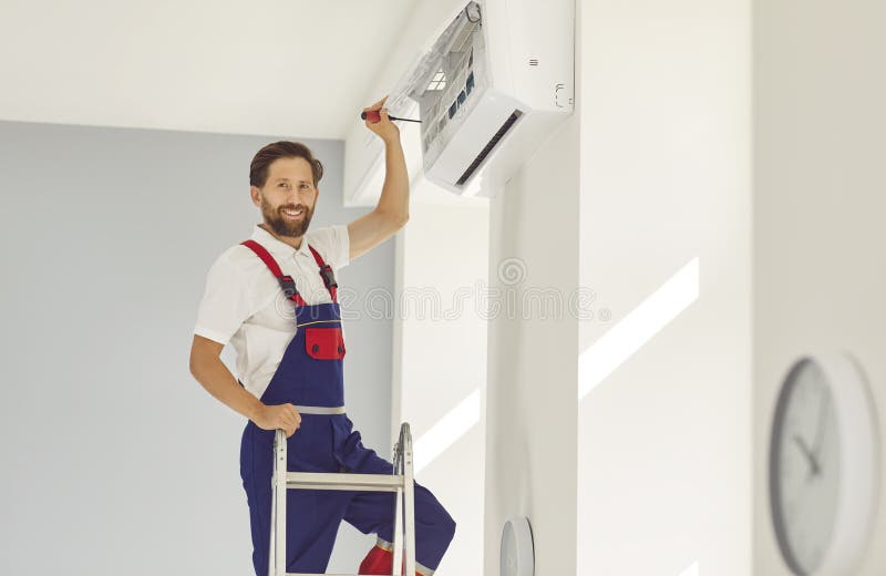 Electricista masculino con destornillador con cara alegre a la cámara durante el mantenimiento del aire acondicionado imagen de archivo libre de regalías