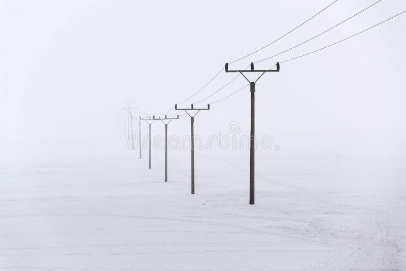 Electricity pylons from distribution power station disappearing in deep fog, winter freezing weather