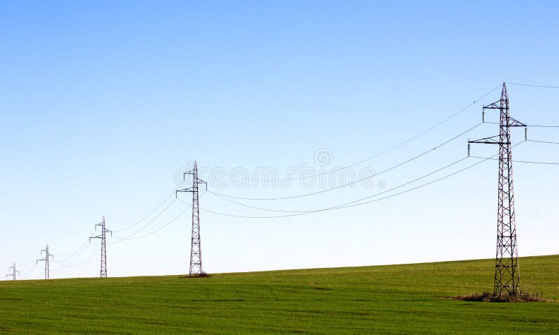 Line of electricity pylons in a field on blue sky. Line of electricity pylons in a field on blue sky