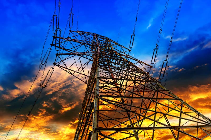 Electricity pylons, power lines and trees silhouetted against a cloudy sky at sunset.