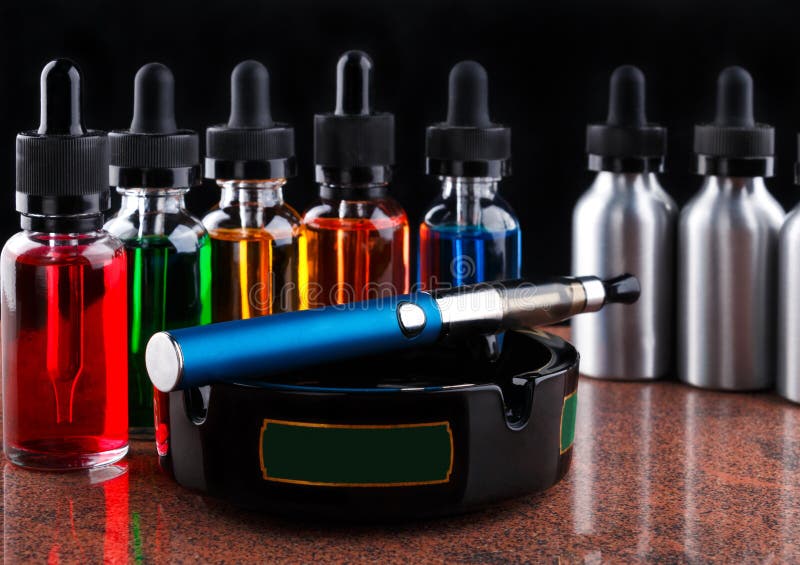 Electronic Cigarette on the Ashtray and Bottles with Vape Liquid on ...