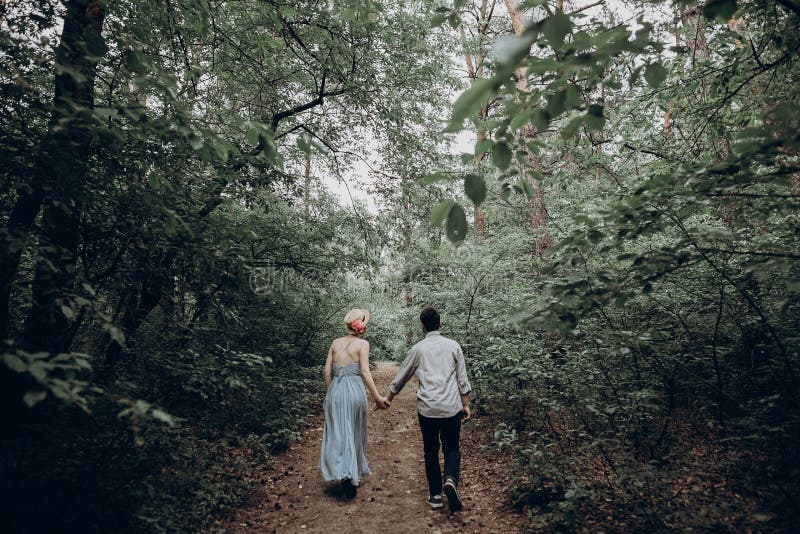 Stylish hipster bride and groom walking in green summer forest. happy couple in love, modern outfit, relaxing at park. girl in dress and straw hat with peony. rustic wedding concept. Stylish hipster bride and groom walking in green summer forest. happy couple in love, modern outfit, relaxing at park. girl in dress and straw hat with peony. rustic wedding concept