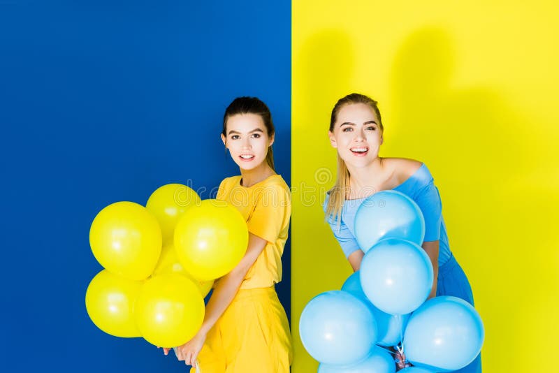 Eleganckie eleganckie kobiety uśmiecha się partyjnych balony na błękicie i trzyma obraz stock Eleganckie eleganckie kobiety uśmiecha się partyjnych balony na błękicie i trzyma obraz stock