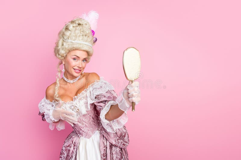 Elegant aristokratisk kvinna i baroque som håller en spegel mot rosa bakgrund som representerar historiskt glamm royaltyfri fotografi